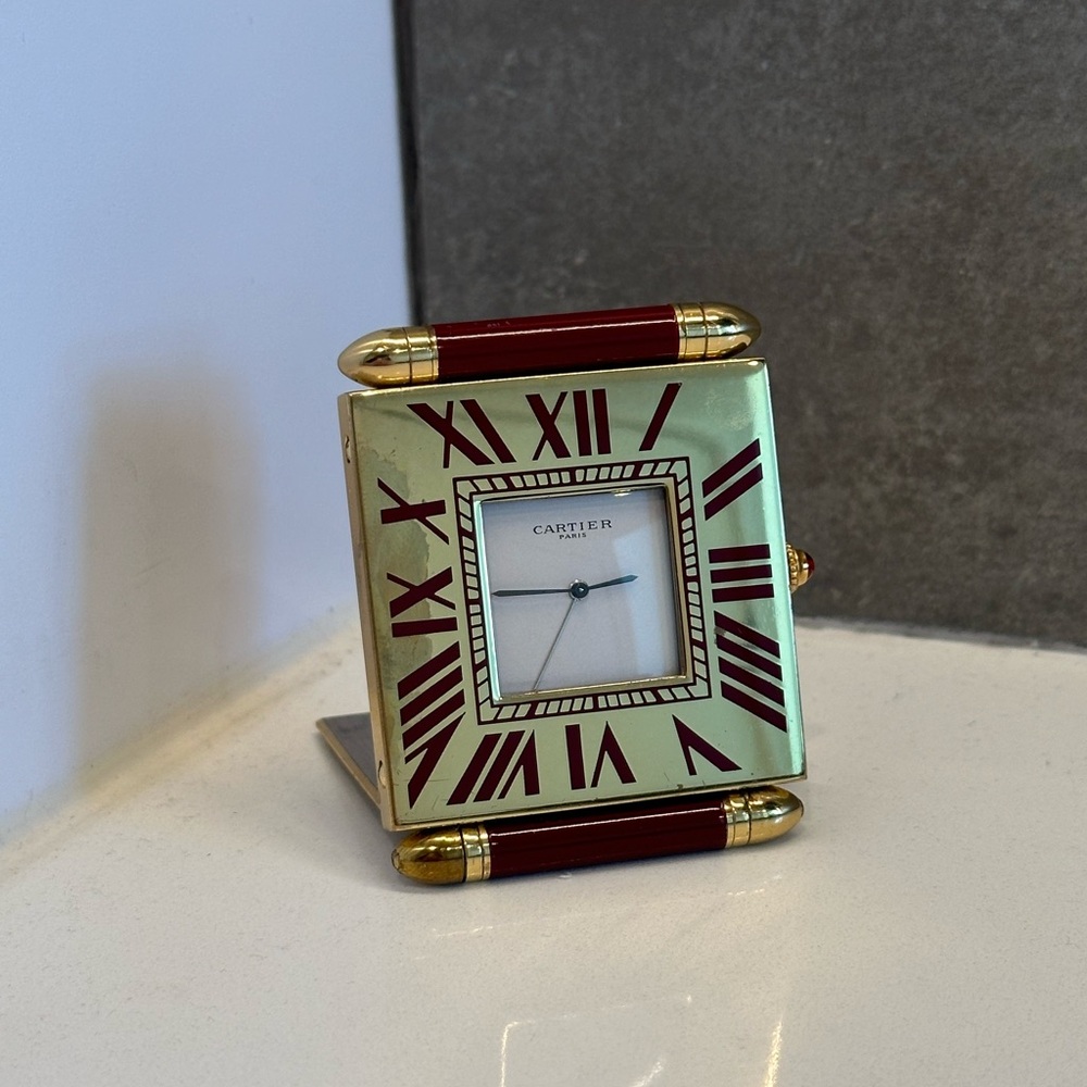 A gold and red Cartier travel size alarm clock. Roman numerals on the bezel.